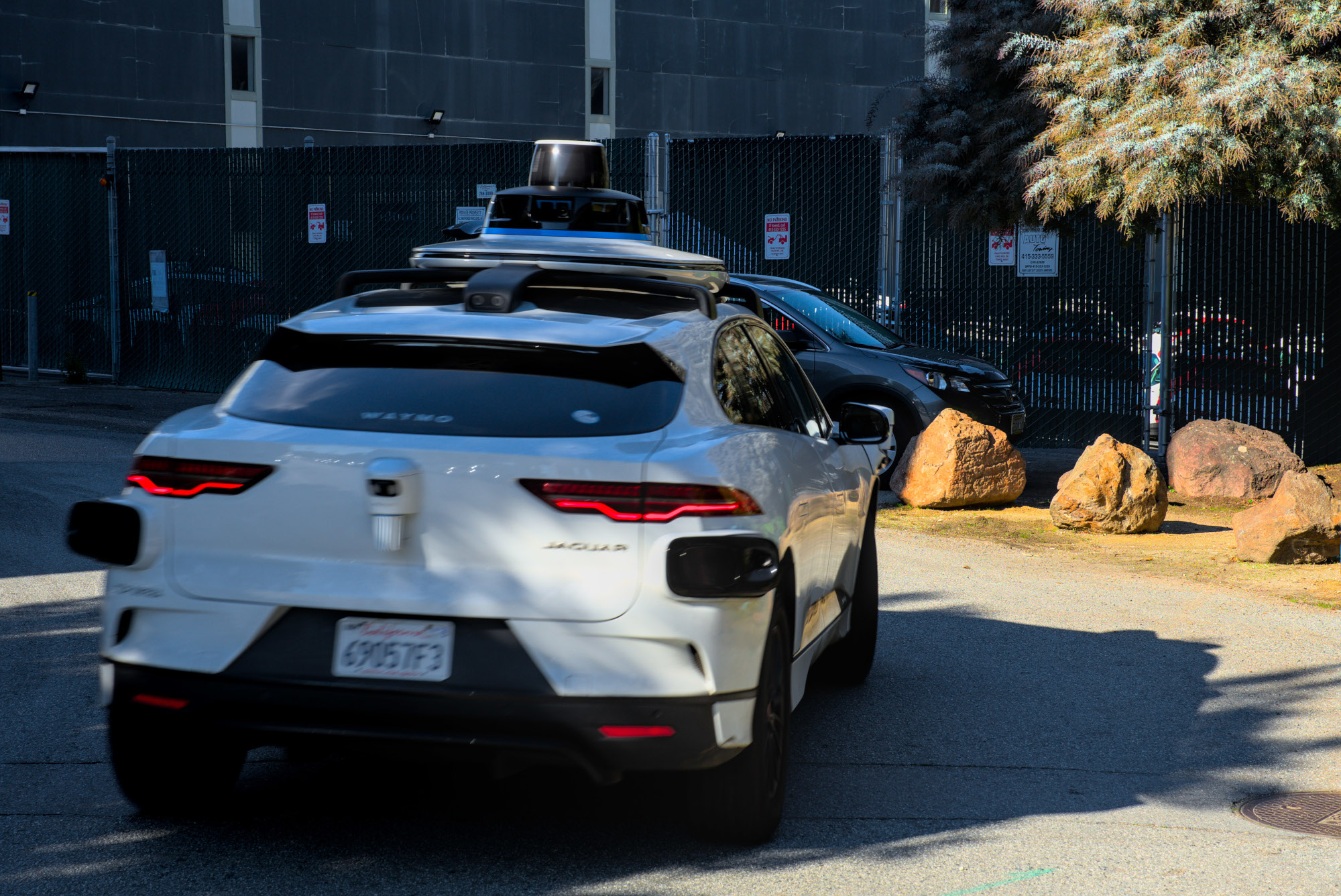An autonomous Waymo car drives by a lot of recently suspended Cruise cars in the northeast corner of Potrero Hill.